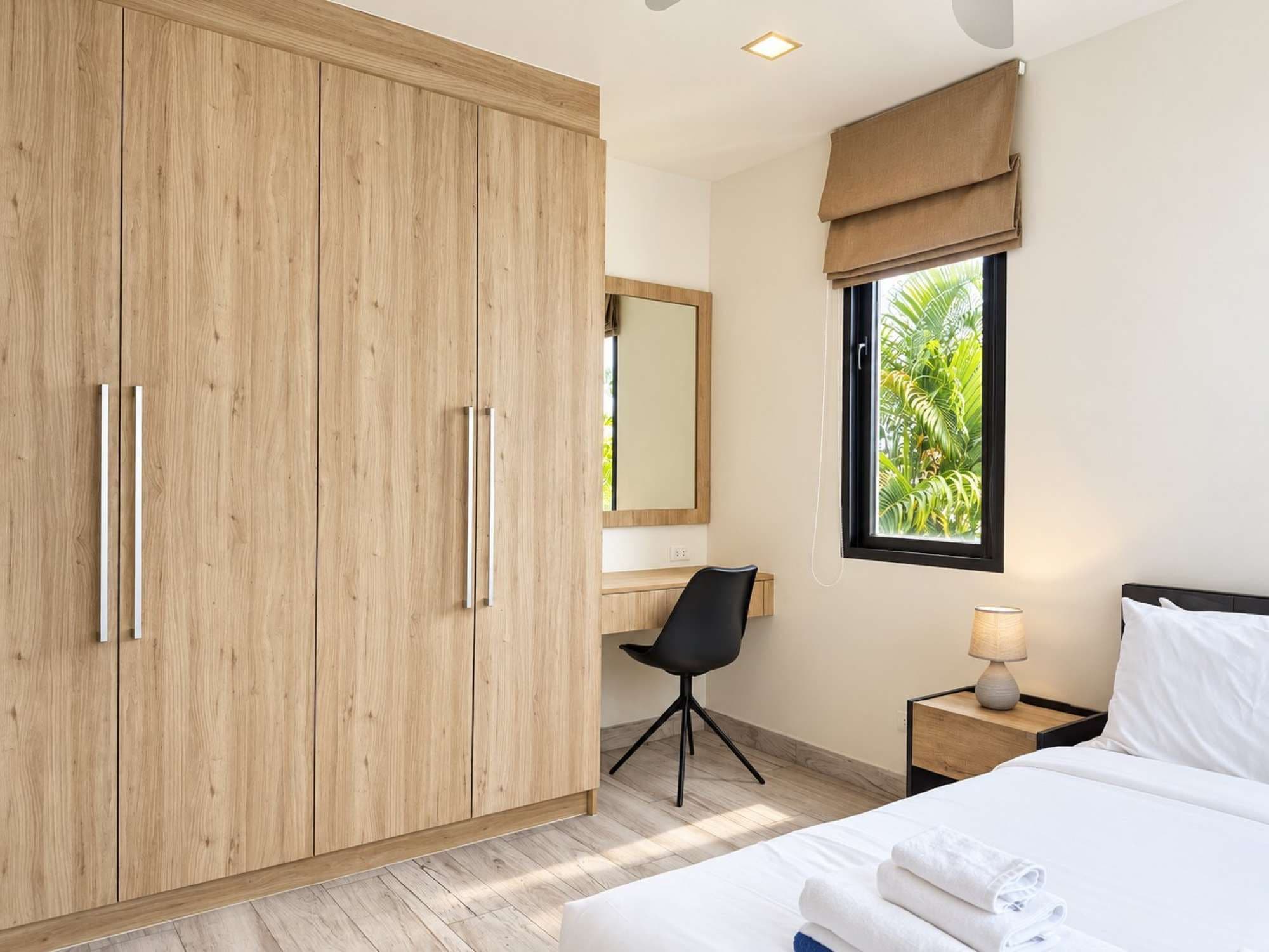 A hotel room with a bed, a desk, a chair, a wardrobe, and a window with a view of greenery.