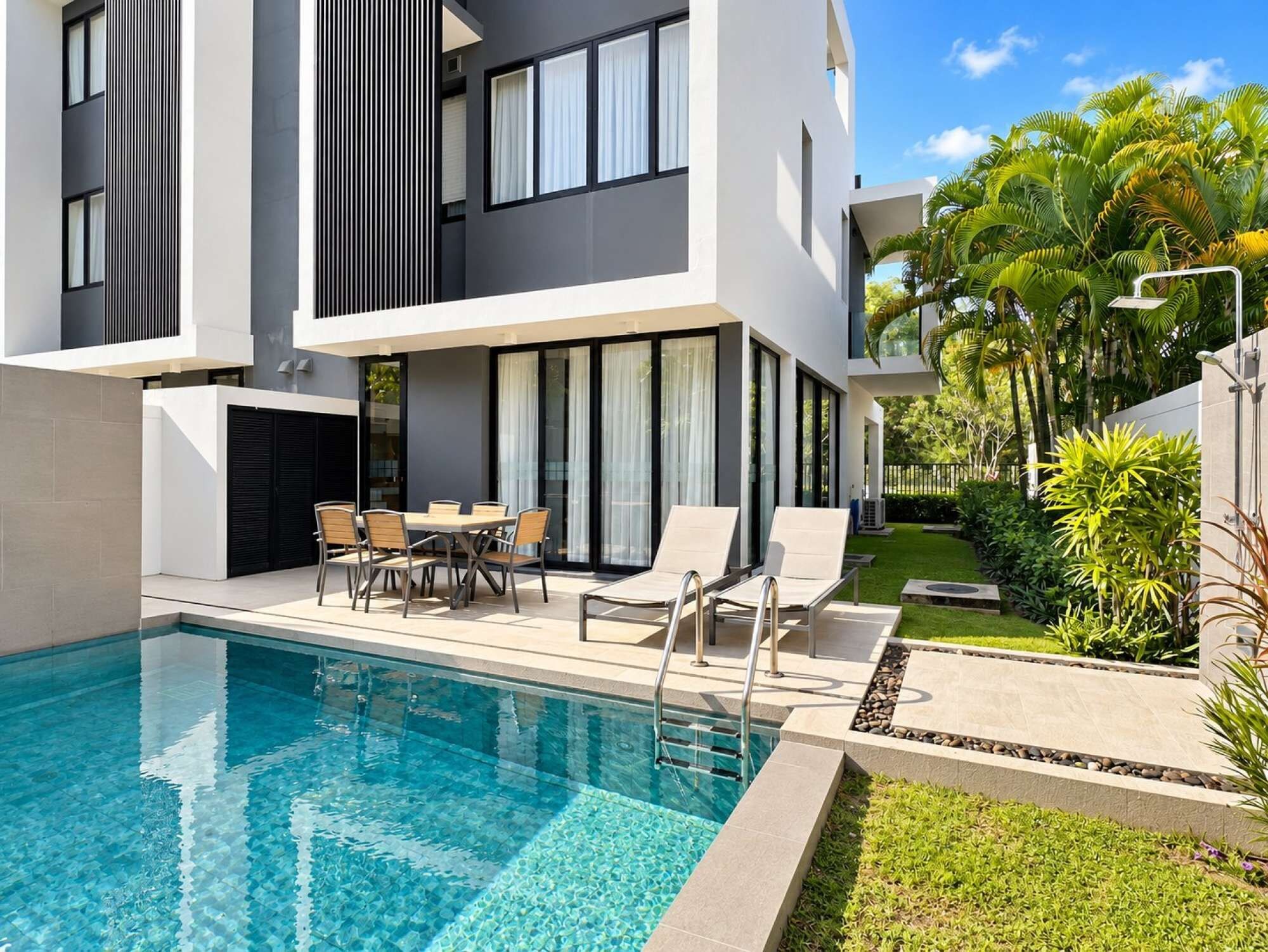 A modern two-story building with a swimming pool, outdoor seating, and lush greenery.