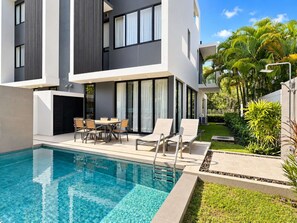 Un bâtiment moderne à deux étages, doté d’une piscine, d’un espace extérieur aménagé et d’une végétation luxuriante.