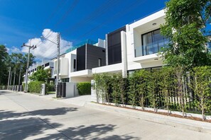 A modern residential building with a clean, minimalist design, featuring a flat roof, large windows, and a well-maintained lawn. - 5bdr Pool Villa LagunaPark 65/40 (Tambon Choeng Thale)