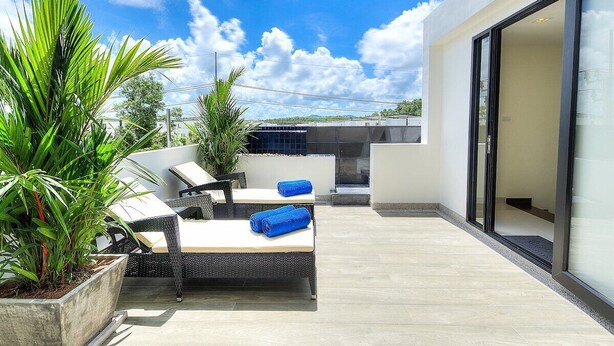 Un espace de détente extérieur moderne, comprenant un canapé et des fauteuils, une grande plante en pot et une porte vitrée donnant sur un patio couvert.