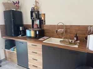 A modern kitchen with a built-in coffee maker, a microwave, a sink with a gold faucet, and wooden cabinetry.