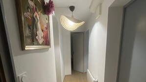 En gang med trægulv, en loftlampe og et billede i ramme på væggen.