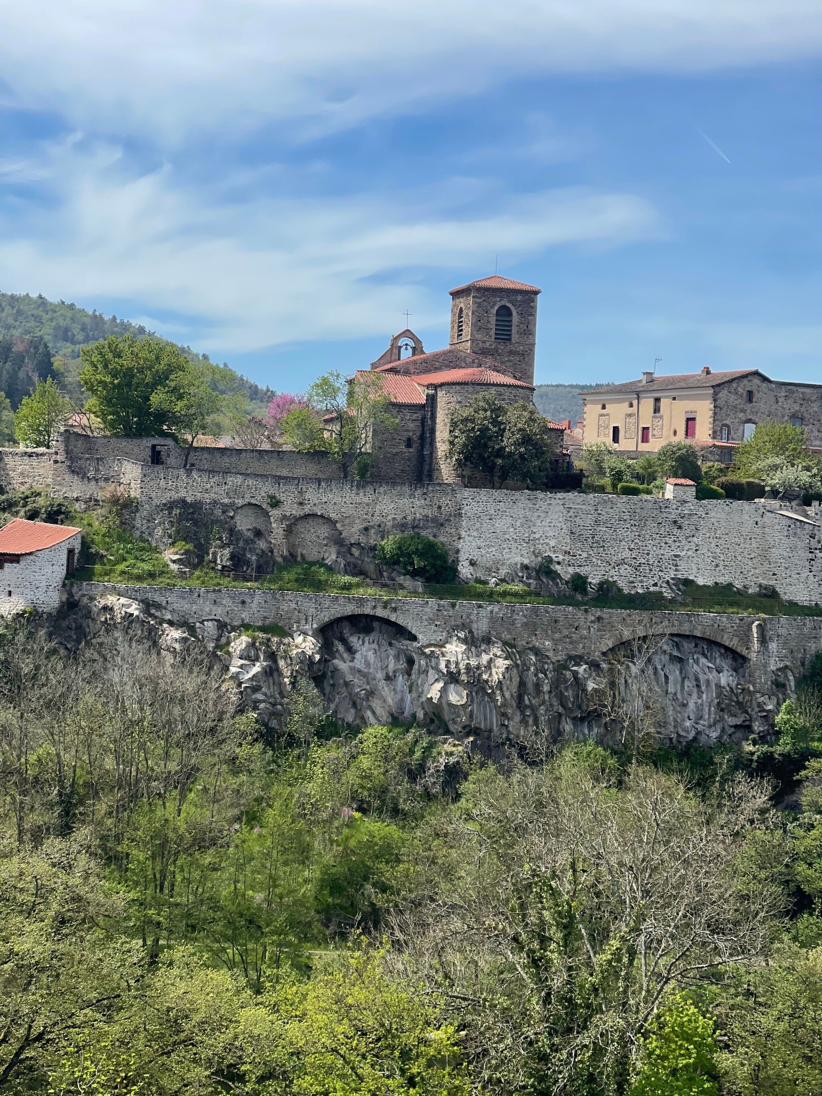 Un puente de piedra histórico, una iglesia con campanario y edificios tradicionales.