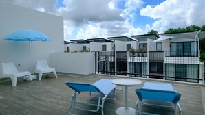 Een terras op het dak met witte lounge stoelen, een blauwe parasol en een witte tafel.