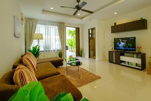 A modern living room with a sofa, TV, and a ceiling fan. - 3BR Townhouse Near Bangtao Beach | Capital Pro (Tambon Choeng Thale)