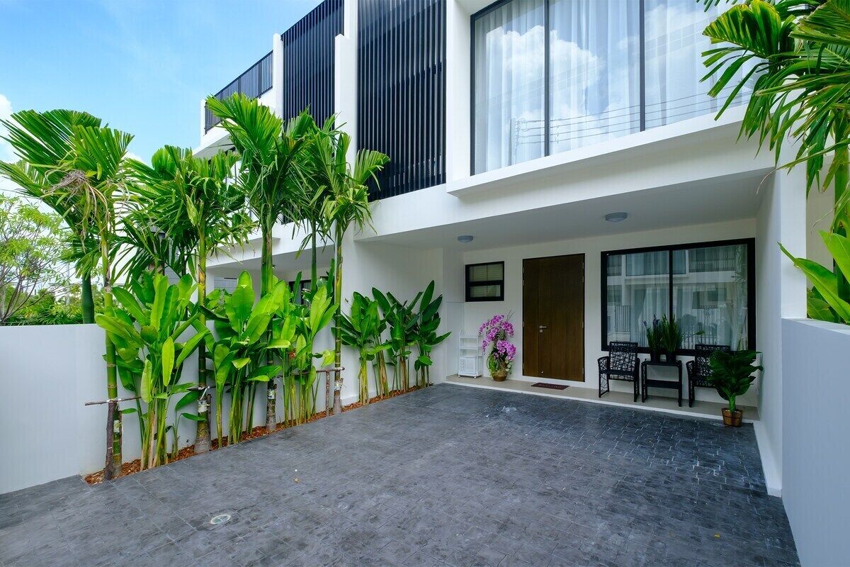 A modern two-story building with a flat roof, large windows, and a paved courtyard.