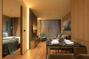 Ein modernes Hotelzimmer mit Bett, einer Sitzecke, einem für zwei Personen gedecktem Esstisch und einem großen Fenster mit Vorhängen.