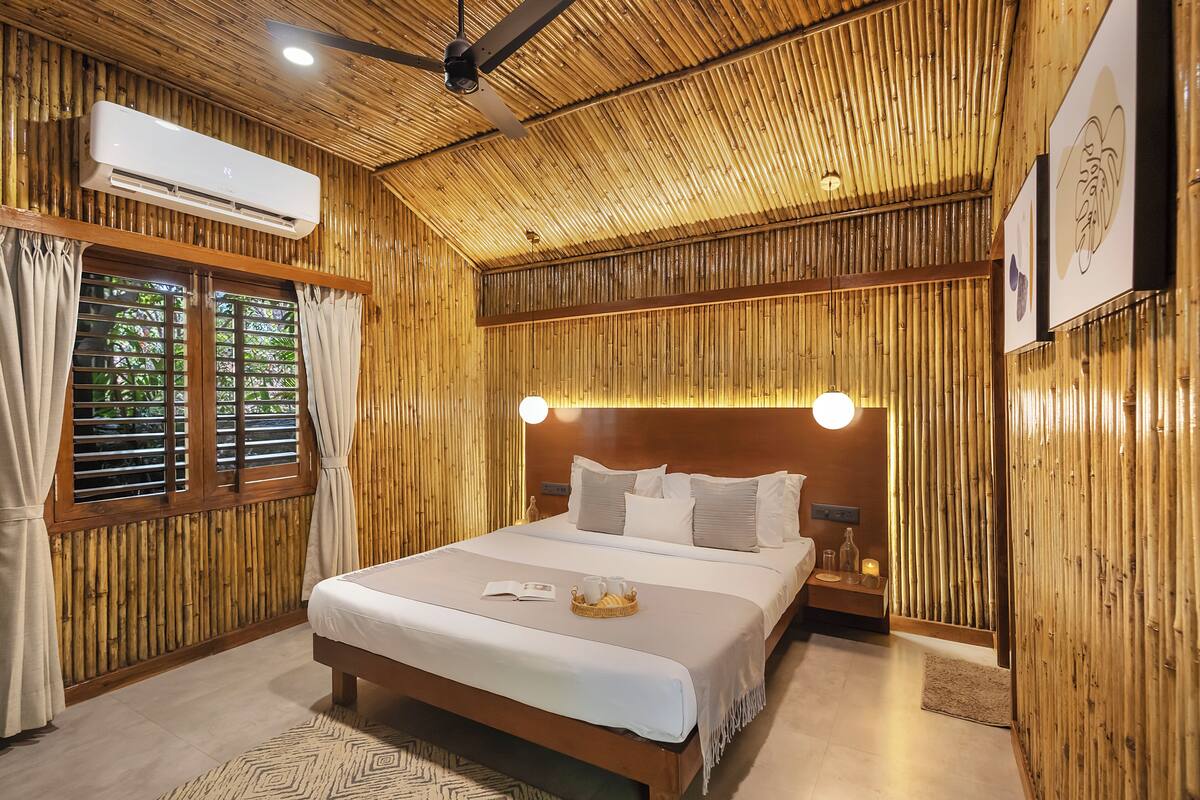 A room with a bed, bedside table, wall-mounted air conditioner, and a window with curtains.