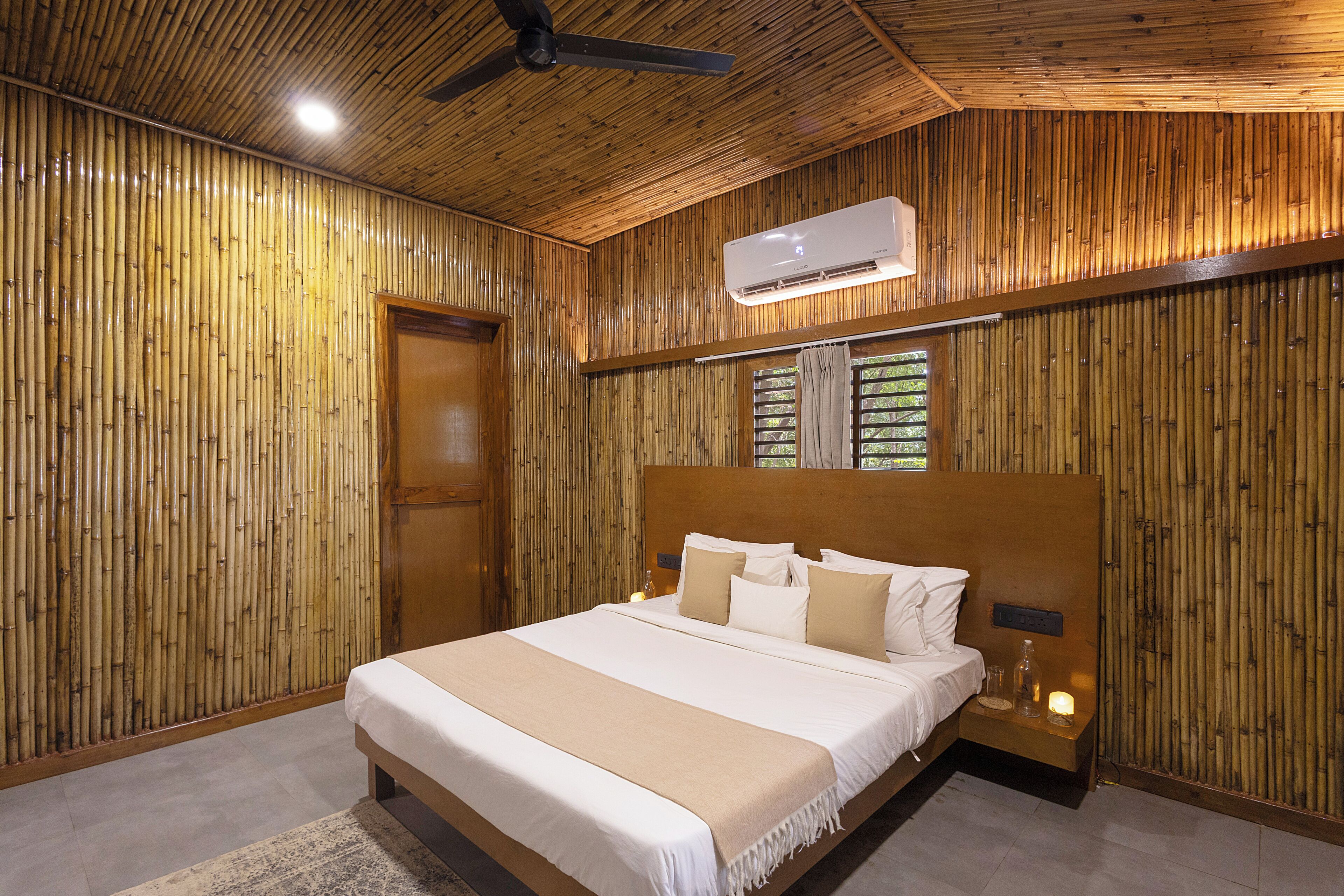 A room with a bed, a ceiling fan, an air conditioning unit, and a window with blinds.