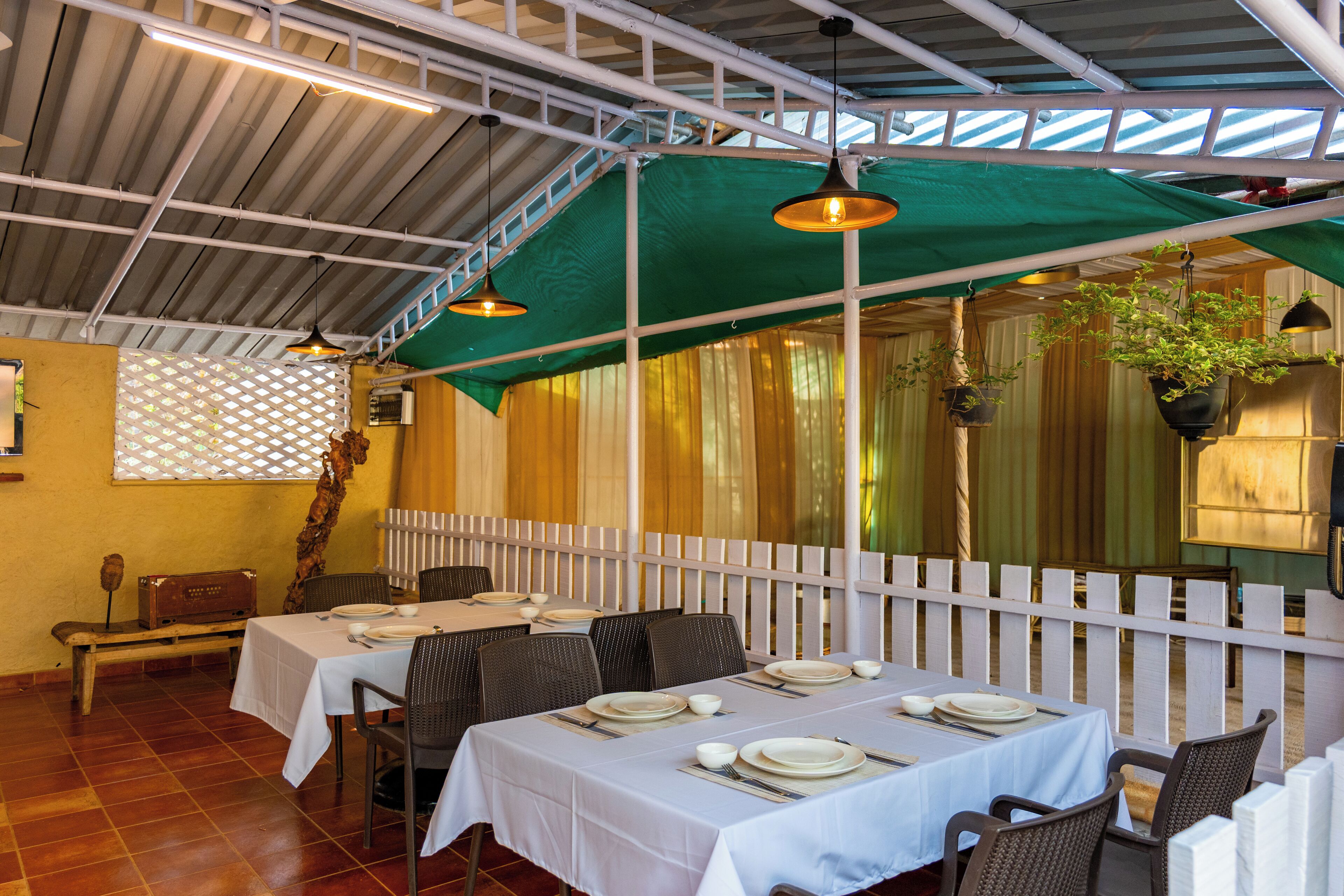 A restaurant with tables set for dining, a white picket fence, and hanging plants.