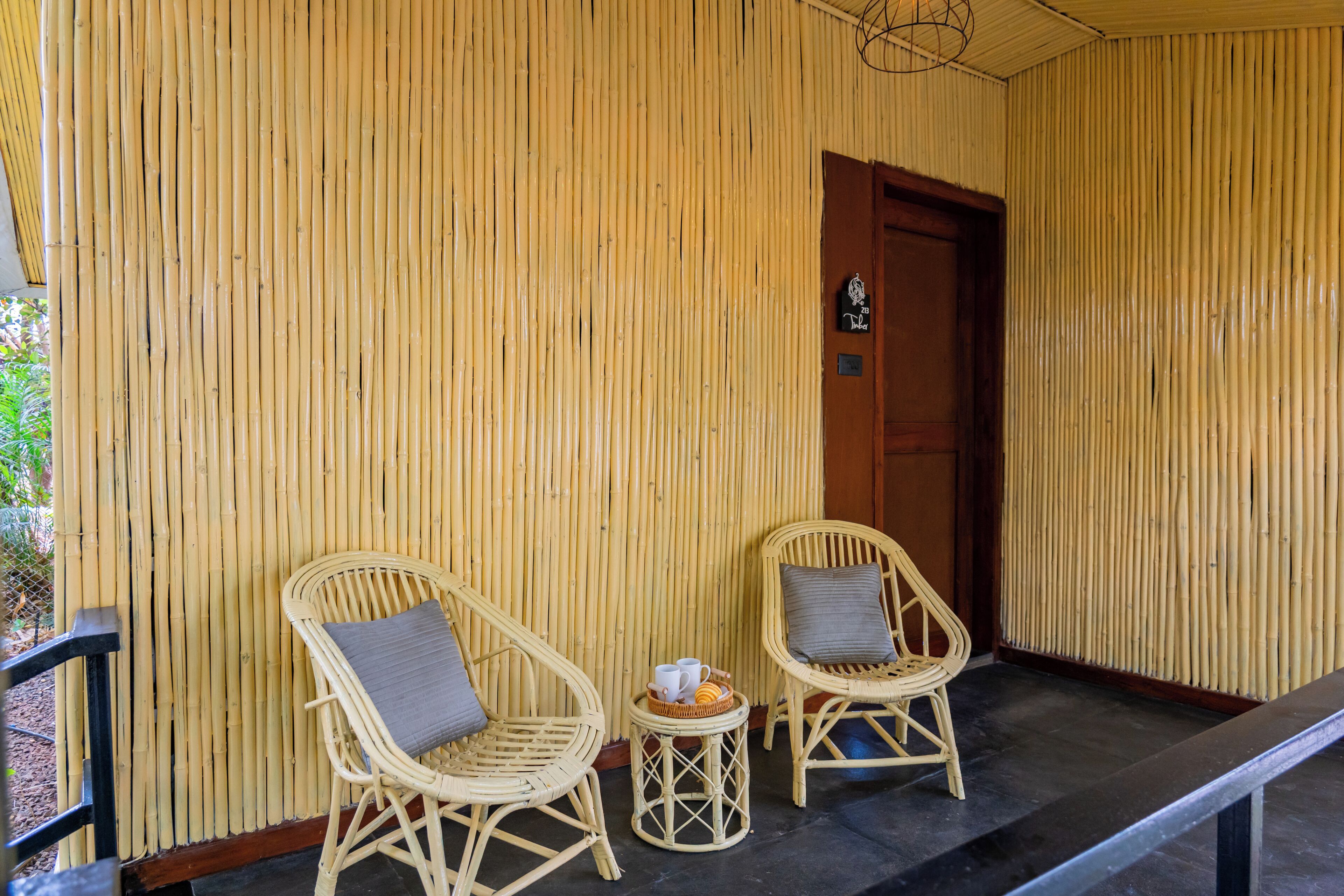 Una habitación con dos sillones de mimbre, una mesita redonda con una taza y una cesta, y una puerta de madera.