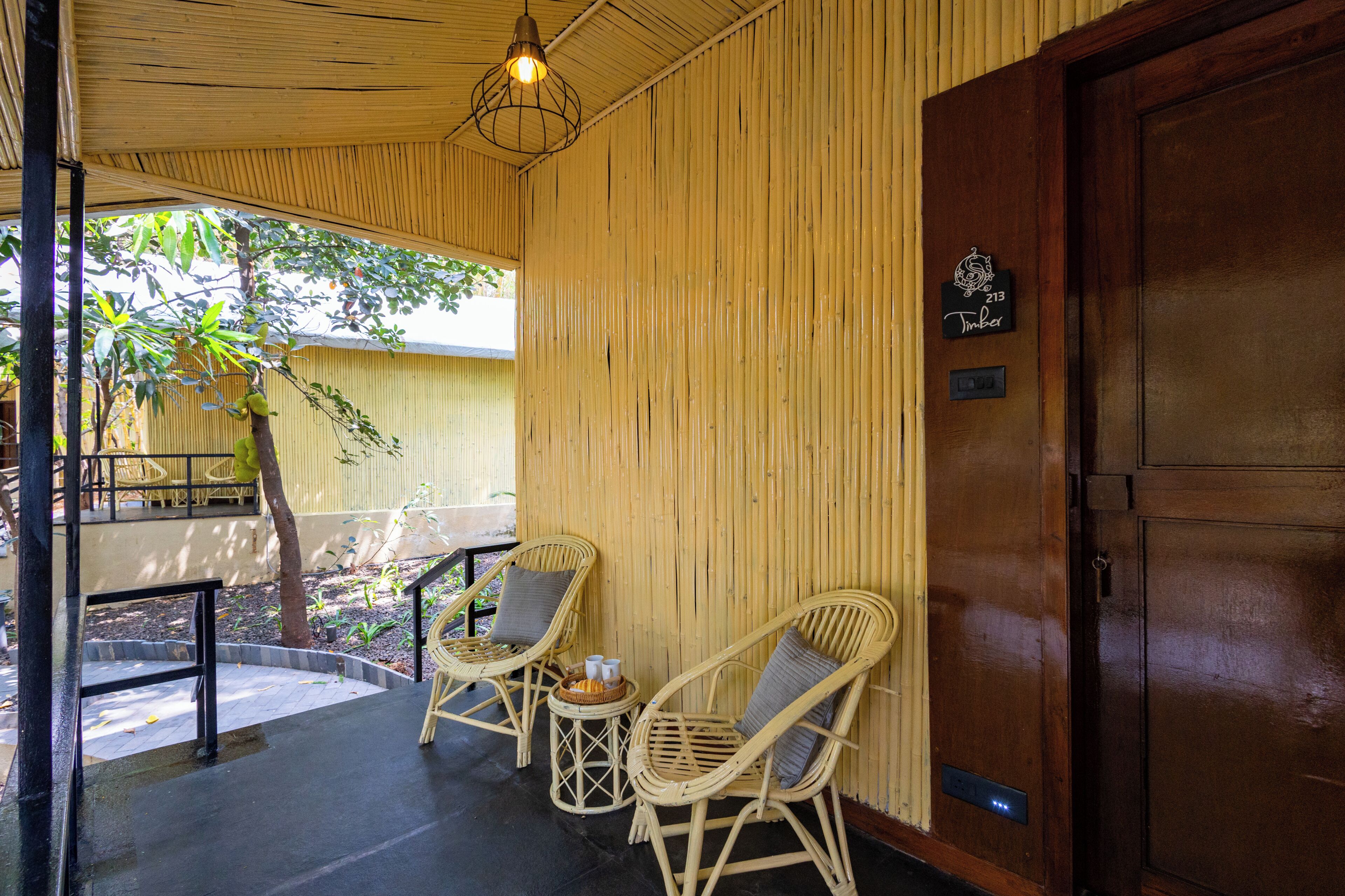 A room with a wooden door, a wicker chair with a cushion, a small table with a basket, and a hanging light fixture.