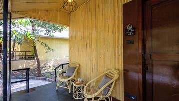 A room with a wooden door, a wicker chair with a cushion, a small table with a basket, and a hanging light fixture.