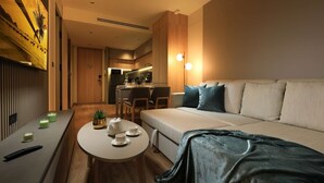 Ein modernes Hotelzimmer mit einer Couch, einem kleinen runden Tisch mit Tee-Service, einer Pflanze und einer Wandpaneele aus Holz.