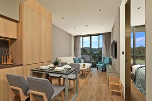 A modern kitchen with wooden cabinets, a dining table set for four, and a large window offering a view of the outdoors. - New 1 bdr Apartment near Layan beach Capital Pro (Choeng Thale)