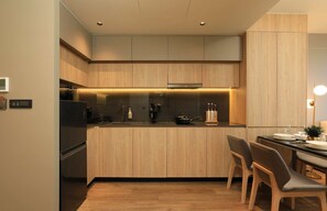 A modern kitchen with wooden cabinets, a built-in stove, and a dining area with chairs. - New 1 bdr Apartment near Layan beach Capital Pro (Choeng Thale)