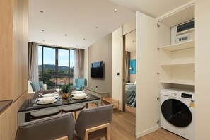 A modern hotel room with a dining area, a TV, a washing machine, and a view of the outdoors. - New 1 bdr Apartment near Layan beach Capital Pro (Choeng Thale)