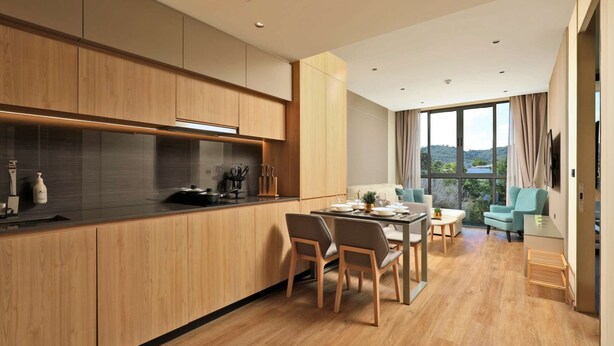 Eine moderne Küche mit Holzausstattung, ein Essbereich mit Tisch und Stühlen sowie ein großes Fenster mit Blick ins Freie.