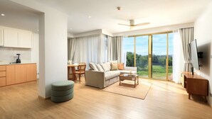 Ein geräumiger Wohnbereich mit Sofa, Couchtisch und Esstisch, großen Schiebeg lass Türen zu einem Balkon sowie eine Küchenzeile mit Schränken und einem Mixer.