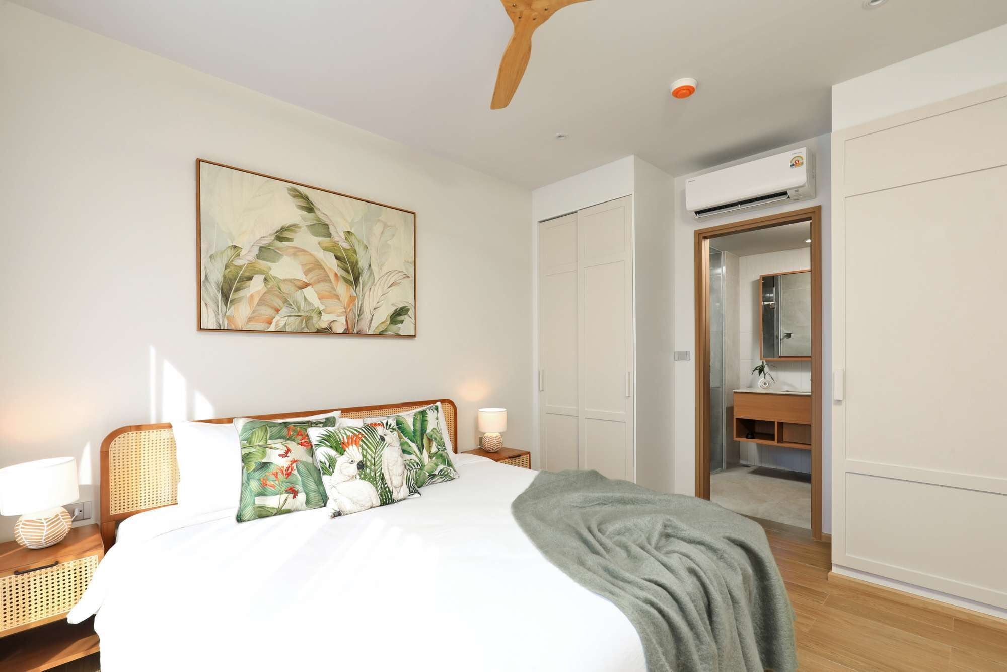 A bedroom with a bed, bedside tables, a nightstand, a wall-mounted air conditioner, a wardrobe, and a door leading to a bathroom.