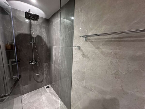 Une salle de bain moderne avec une douche à parois de verre, un porte-serviettes et un mur recouvert de carreaux de marbre.
