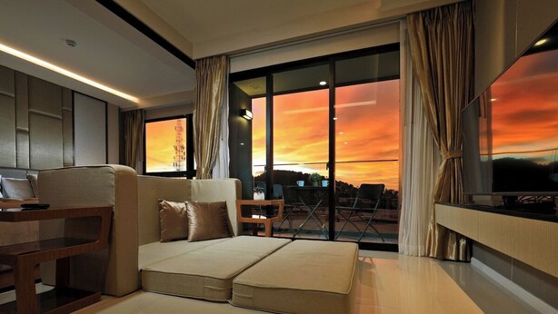 Habitación de hotel moderna con una cama grande, un escritorio y vistas a un atardecer a través de amplias ventanas.