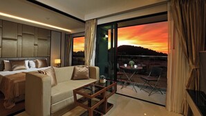 Una habitación de hotel moderna con cama, sofá y balcón con vistas al atardecer.