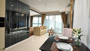 Habitación de hotel moderna con separador de vidrio, un sofá, una mesa de comedor para dos personas y vistas a la ciudad.