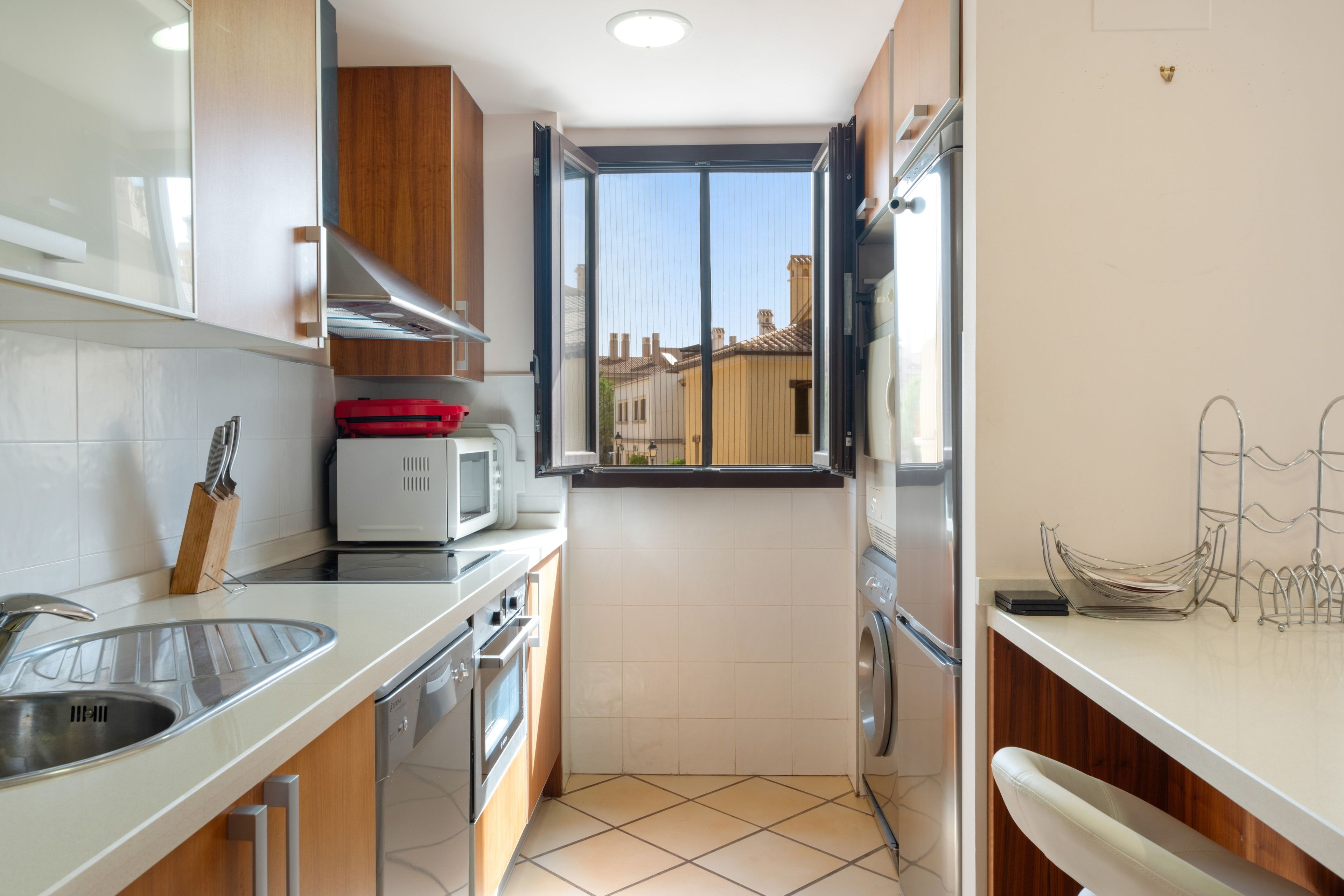 Una cocina compacta con ventana, electrodomésticos de acero inoxidable y salpicadero de azulejos.