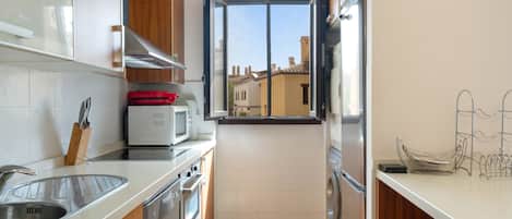 Una cocina compacta con ventana, electrodomésticos de acero inoxidable y salpicadero de azulejos.