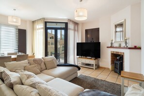 Ein modernes Wohnzimmer mit Sofa, Fernseher, Kamin und Blick ins Freie.