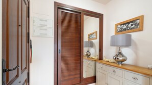 Une pièce avec une porte en bois, un miroir, une commode et une lampe posée sur une étagère en bois.