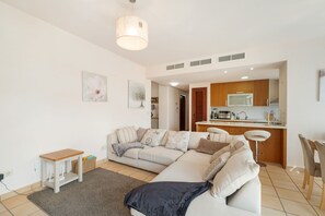 Ein modernes Wohnzimmer mit einer Couch, einem kleinen Tisch und einer Küchenzeile im Hintergrund.