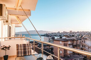 Un balcon avec une balustrade, un pot de fleurs et une vue sur le paysage urbain et la mer.