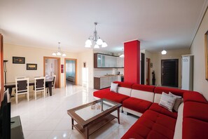 A modern living room with a red sofa, a glass coffee table, and a dining area with chairs and a table. - Albania Dream Saranda Apartments (Saranda)