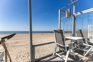 A beach view from a covered deck with a table and chairs, a hanging lantern, and a wooden walkway leading to the beach. - Slaapstrandhuisje - Strand Dishoek 37 I Dishoek (Vlissingen)