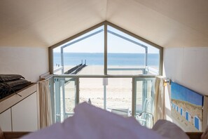 A room with a large window overlooking a beach, a bed, and a painting on the wall. - Slaapstrandhuisje - Strand Dishoek 37 I Dishoek (Vlissingen)