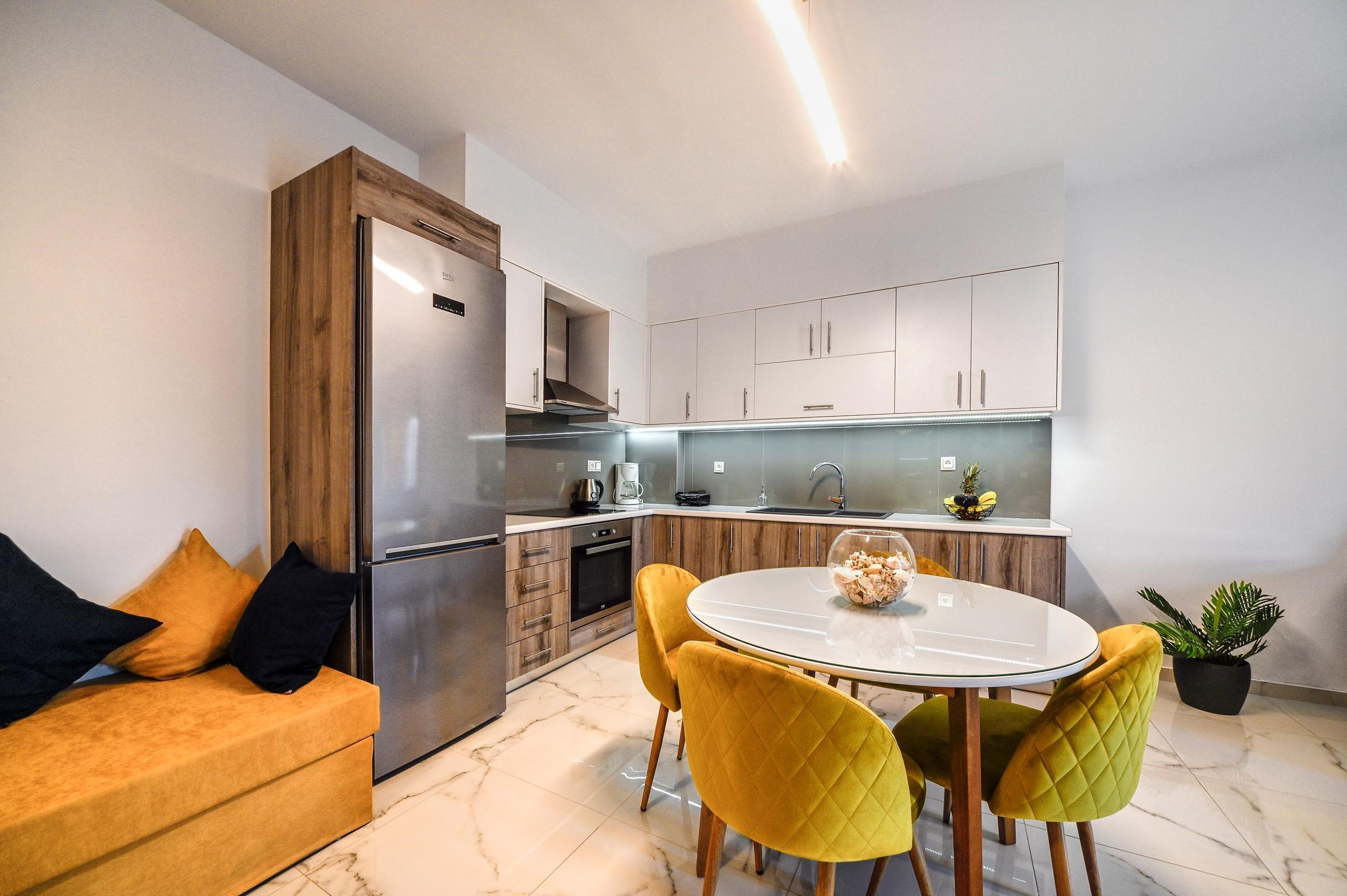 Una cucina moderna con forno integrato, frigorifero e zona pranzo con tavolo rotondo e sedie gialle.