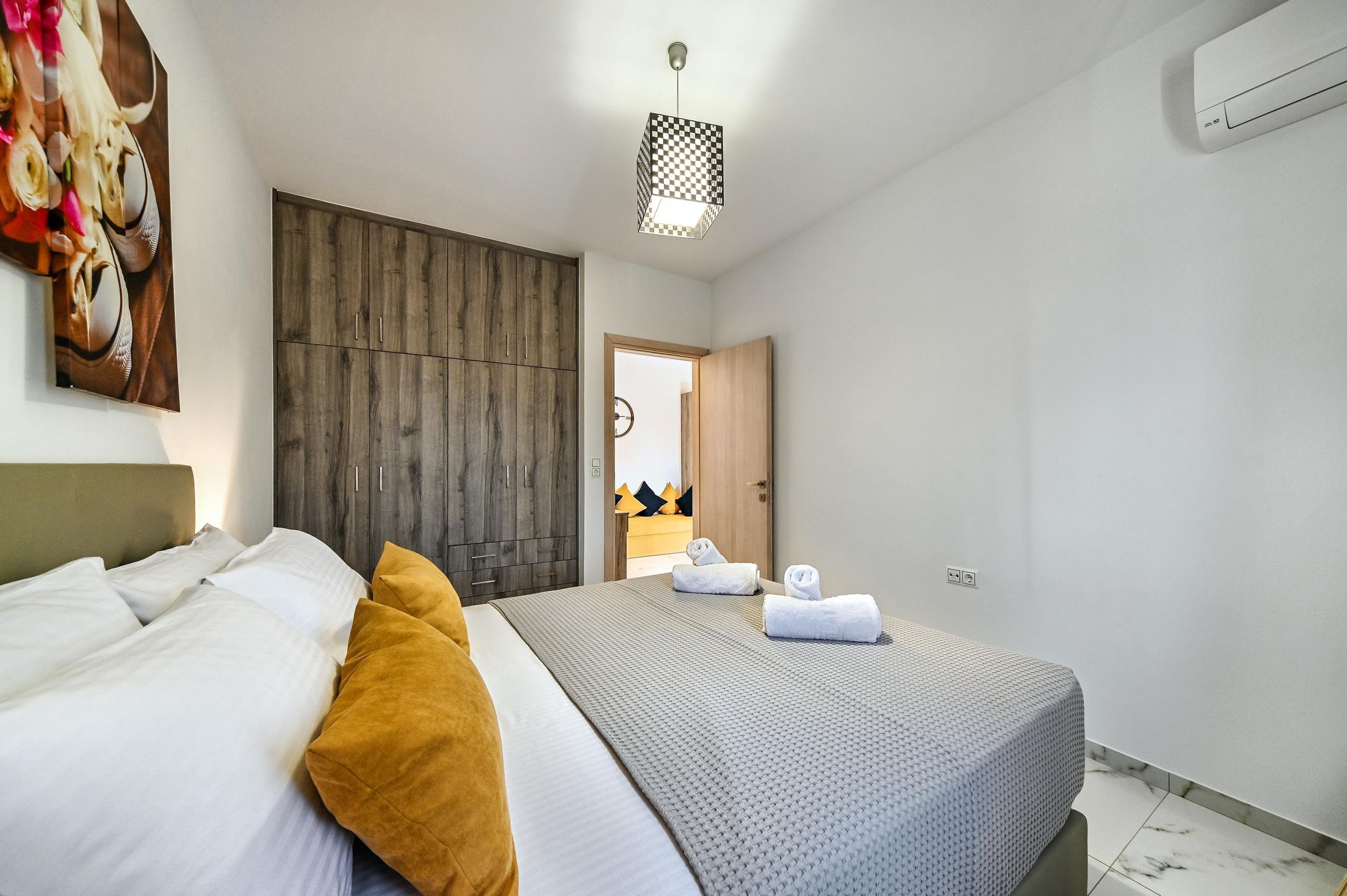 A hotel room with a bed, a wardrobe, a hanging light fixture, and an air conditioning unit.