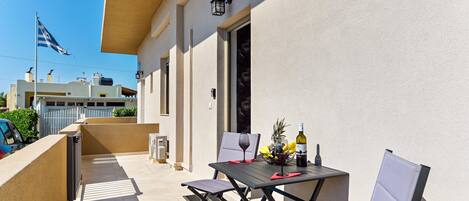 An outdoor balcony with a table, chairs, a bottle of wine, and a flag.