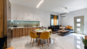 A modern kitchen with a dining area, a living room with a sofa and coffee table, and a door with a window. - Seaside Apartment 1 by Cretanhouses (Hersonissos)