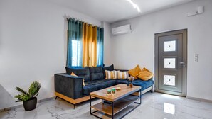 A modern living room with a dark sofa, a wooden coffee table, a potted plant, and a door with a window. - Seaside Apartment 1 by Cretanhouses (Hersonissos)