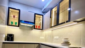 A modern kitchen with white cabinets, a built-in oven, and a ceiling fan. - AvyAm Blue Terrace Apartment in New Delhi! Room-2 (Superior) (New Delhi)
