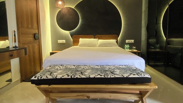 A modern bedroom with a bed, bedside tables, a circular wall light, and a wooden bench. - AvyAm Blue Terrace Apartment in New Delhi! Room-2 (Superior) (New Delhi)