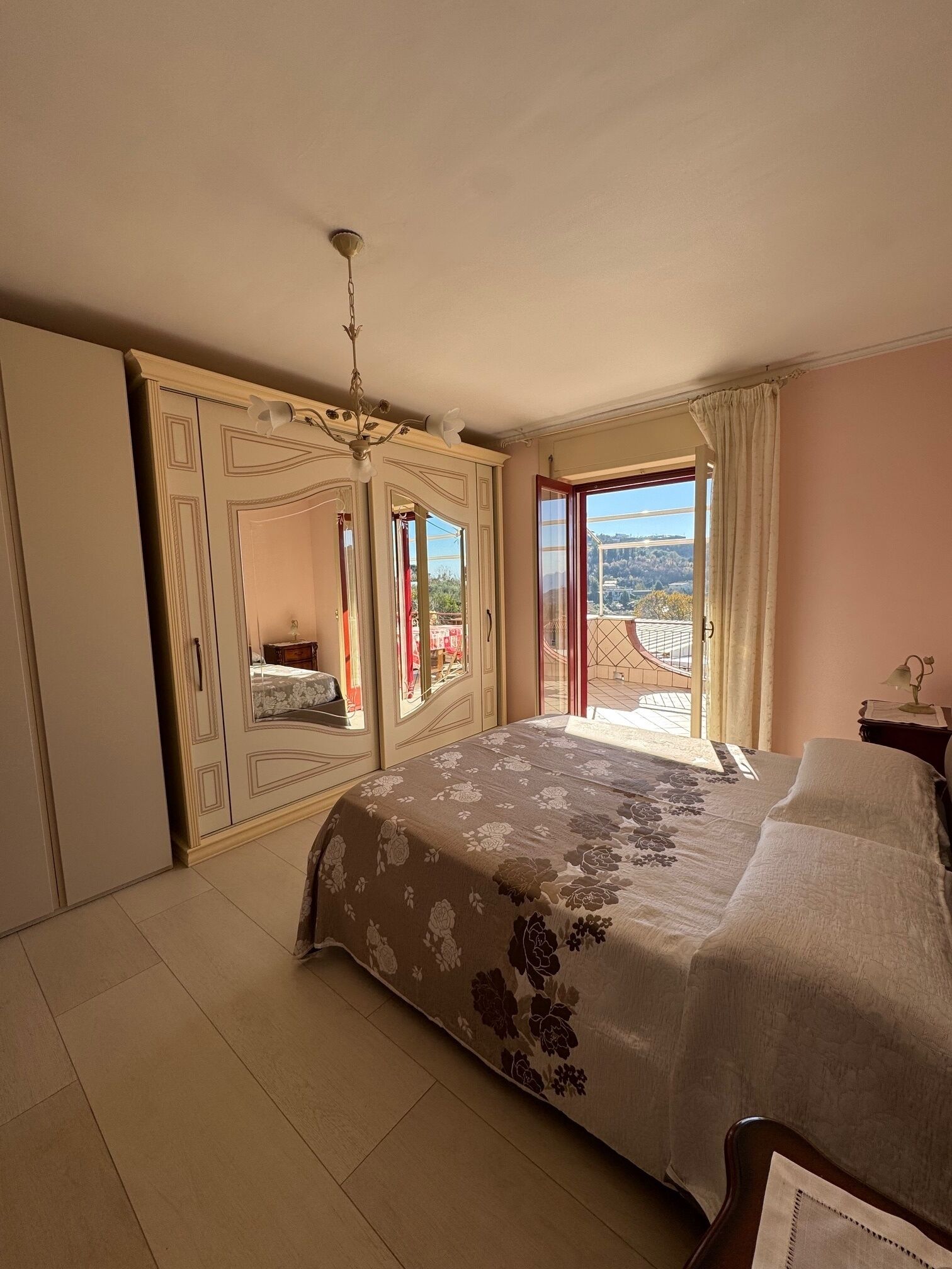 A bedroom with a bed, a wardrobe, a mirror, and a balcony with a view.