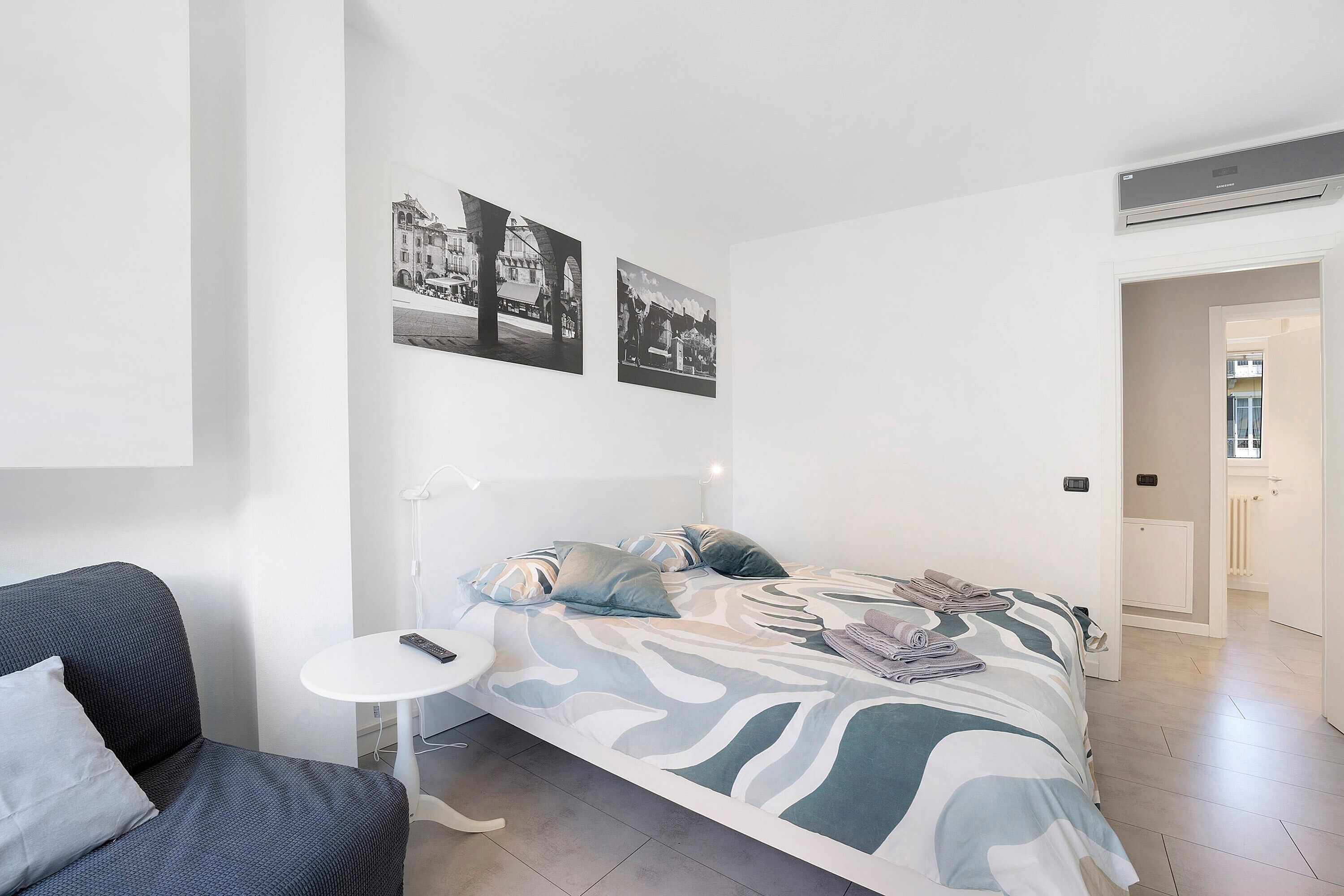 A modern hotel room with a bed, a small table, a chair, and a wall-mounted air conditioner.