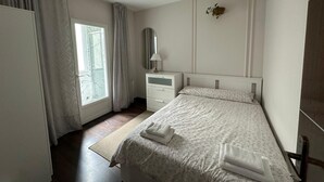 Ein Schlafzimmer mit einem Bett, einem Nachttisch, einem Spiegel und einem Fenster mit Vorhängen.