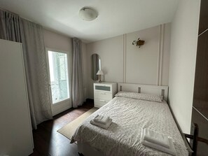 A bedroom with a bed, a bedside table, a mirror, and a window with curtains. - Sagrada Familia flat for 9 pple! (Barcelona)