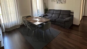 Ein modernes Wohnzimmer mit Esstisch, grauem Sofa und einem großen Fenster mit Vorhängen.